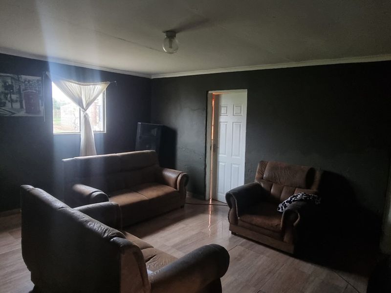 A living room featuring tiled flooring and dark-painted walls, requiring updated lighting and finishes to improve the overall ambiance.