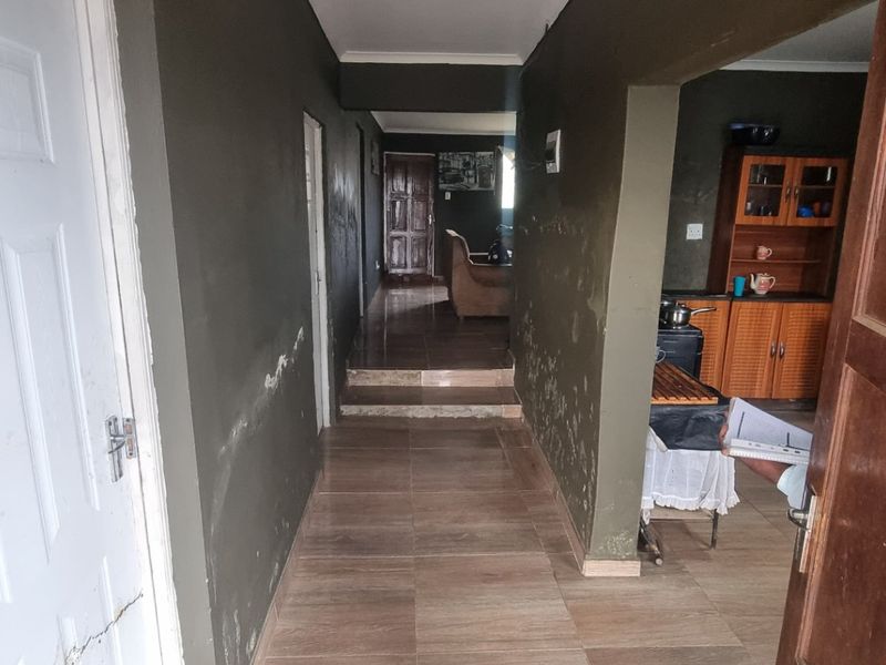 A hallway featuring tiled flooring and access to adjacent rooms, showing signs of wear on the wall surfaces.