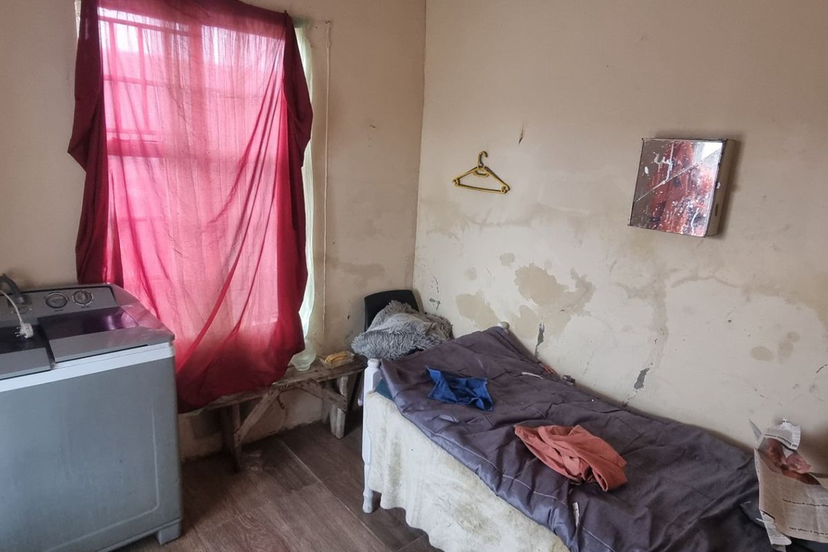 A bedroom space featuring laminate flooring and a window, currently requiring significant wall repairs and cosmetic updates to improve its overall condition.