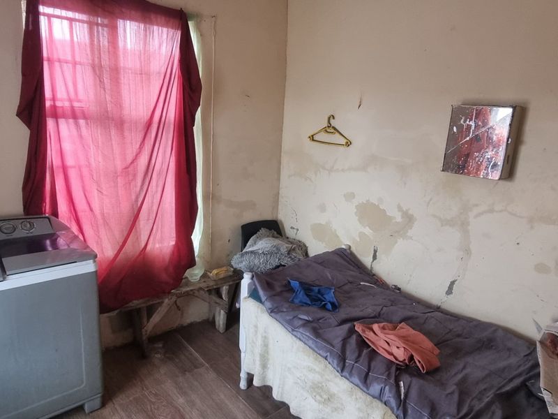 A bedroom space featuring laminate flooring and a window, currently requiring significant wall repairs and cosmetic updates to improve its overall condition.