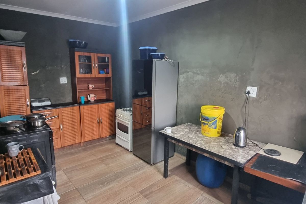 A functional kitchen space featuring wooden cabinetry, tiled flooring, and a freestanding stove, currently requiring wall finishing and aesthetic updates.