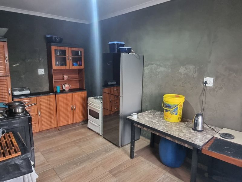 A functional kitchen space featuring wooden cabinetry, tiled flooring, and a freestanding stove, currently requiring wall finishing and aesthetic updates.