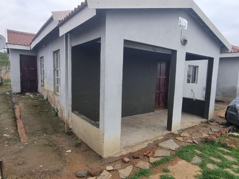 Front elevation of a single-story house featuring a covered porch, tiled roof, and boundary wall, requiring exterior maintenance and landscaping improvements.