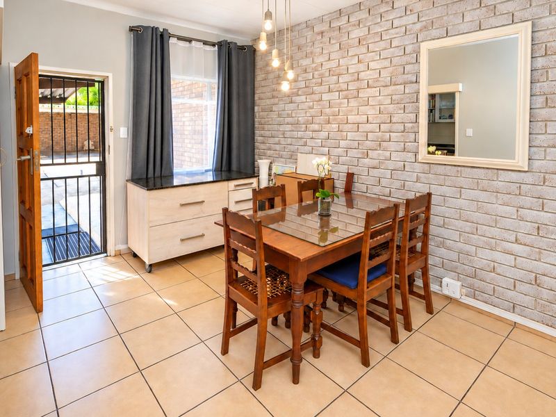 Dining area featuring an exposed brick wall, ceramic floor tiles, and direct access to the exterior through a security gate.