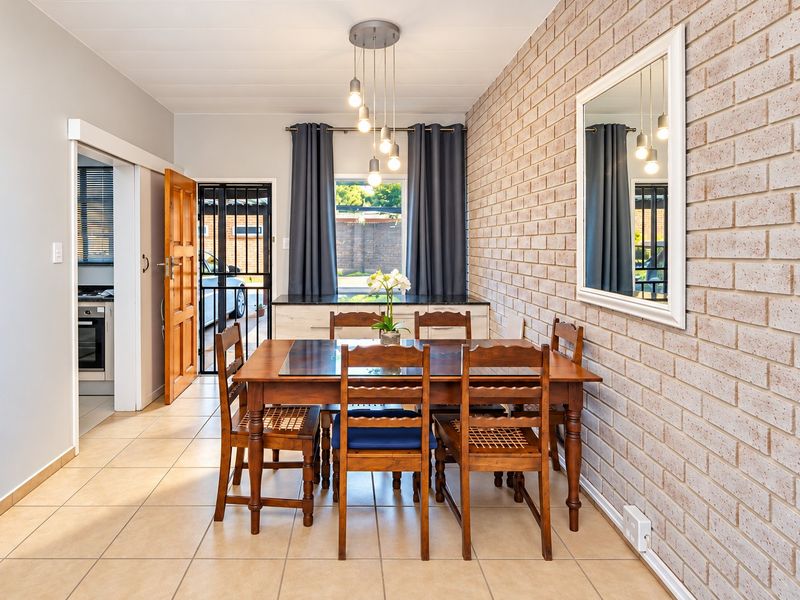 A bright dining area featuring an exposed brick feature wall, tiled flooring, and modern pendant lighting, with direct access to the kitchen and exterior.