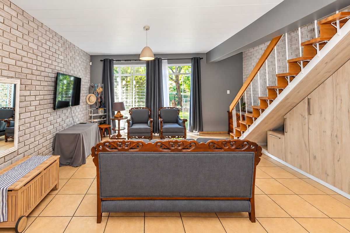 Spacious living room featuring exposed brick walls, tiled flooring, and a wooden staircase with integrated under-stair storage cabinetry.