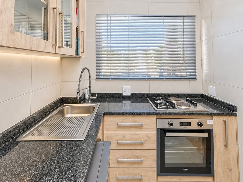 Modern kitchen featuring granite countertops, light wood veneer cabinetry, built-in oven, gas hob, and stainless steel sink with under-cabinet lighting.