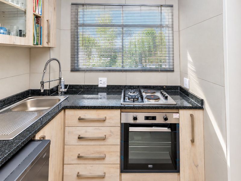 A modern, compact kitchen featuring light wood cabinetry, granite countertops, a combination gas and electric hob, and a built-in oven.