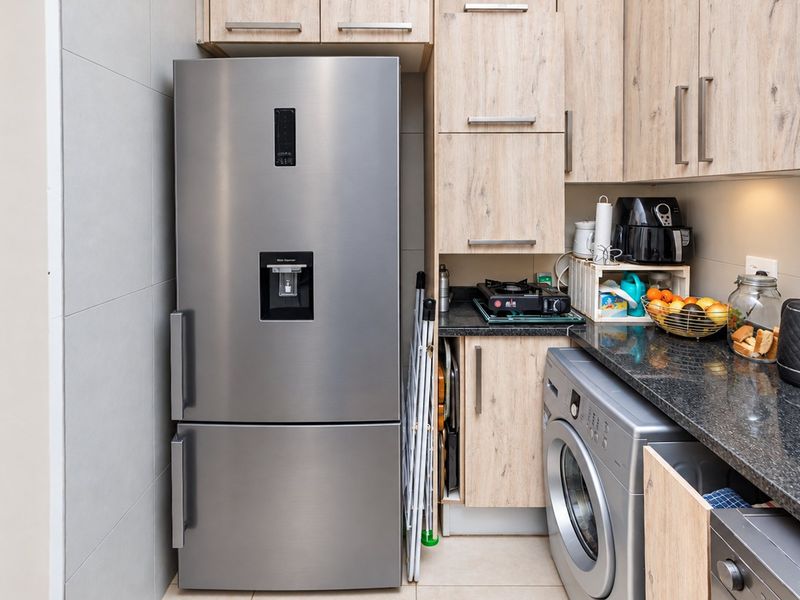 A compact and functional scullery featuring modern wood-finish cabinetry, granite countertops, and integrated laundry appliances, providing efficient utility space.