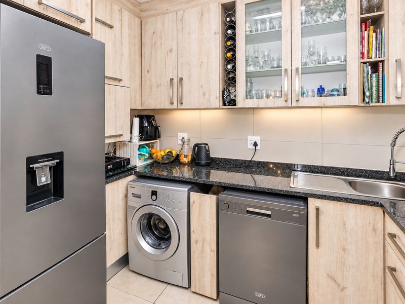 Modern kitchen featuring light wood-finish cabinetry, granite countertops, tiled backsplash, and integrated space for laundry and dishwashing appliances.