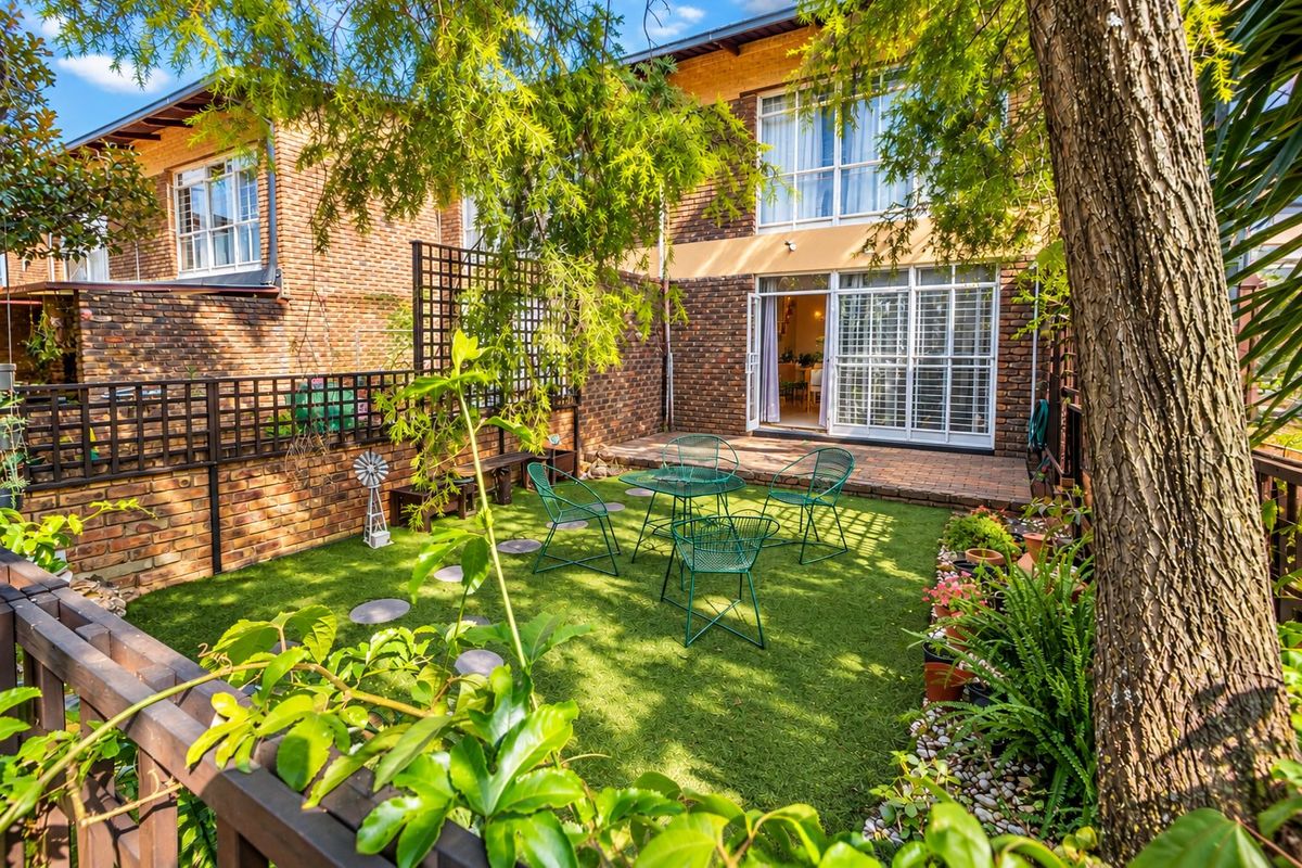 A private rear garden featuring a paved patio area, artificial lawn, and established landscaping, accessible via sliding glass doors from the townhouse.