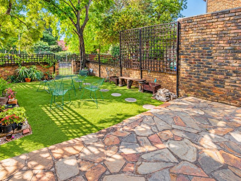 A private rear garden featuring a stone-paved patio area, artificial grass lawn, and secure face brick boundary walls with decorative trellis fencing.