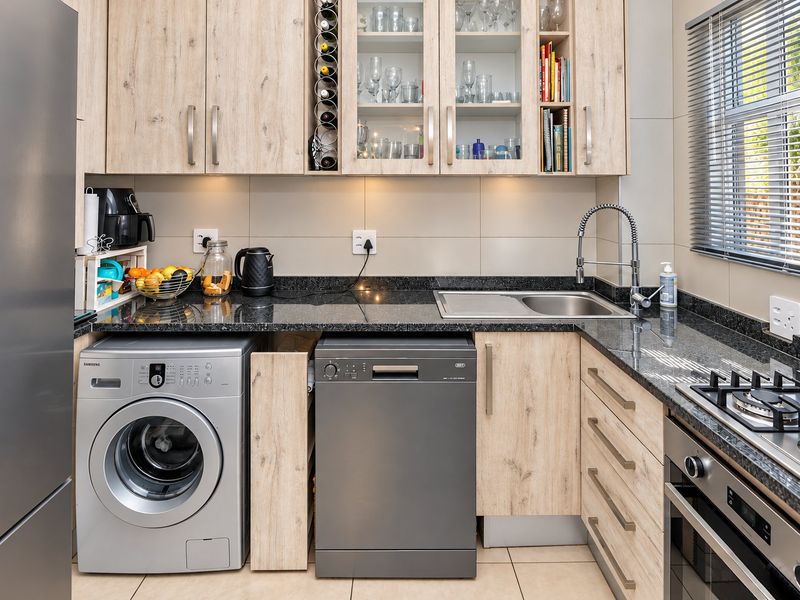Modern kitchen featuring light wood-grain cabinetry, dark granite countertops, integrated appliances, and a functional layout with ample storage and task lighting.