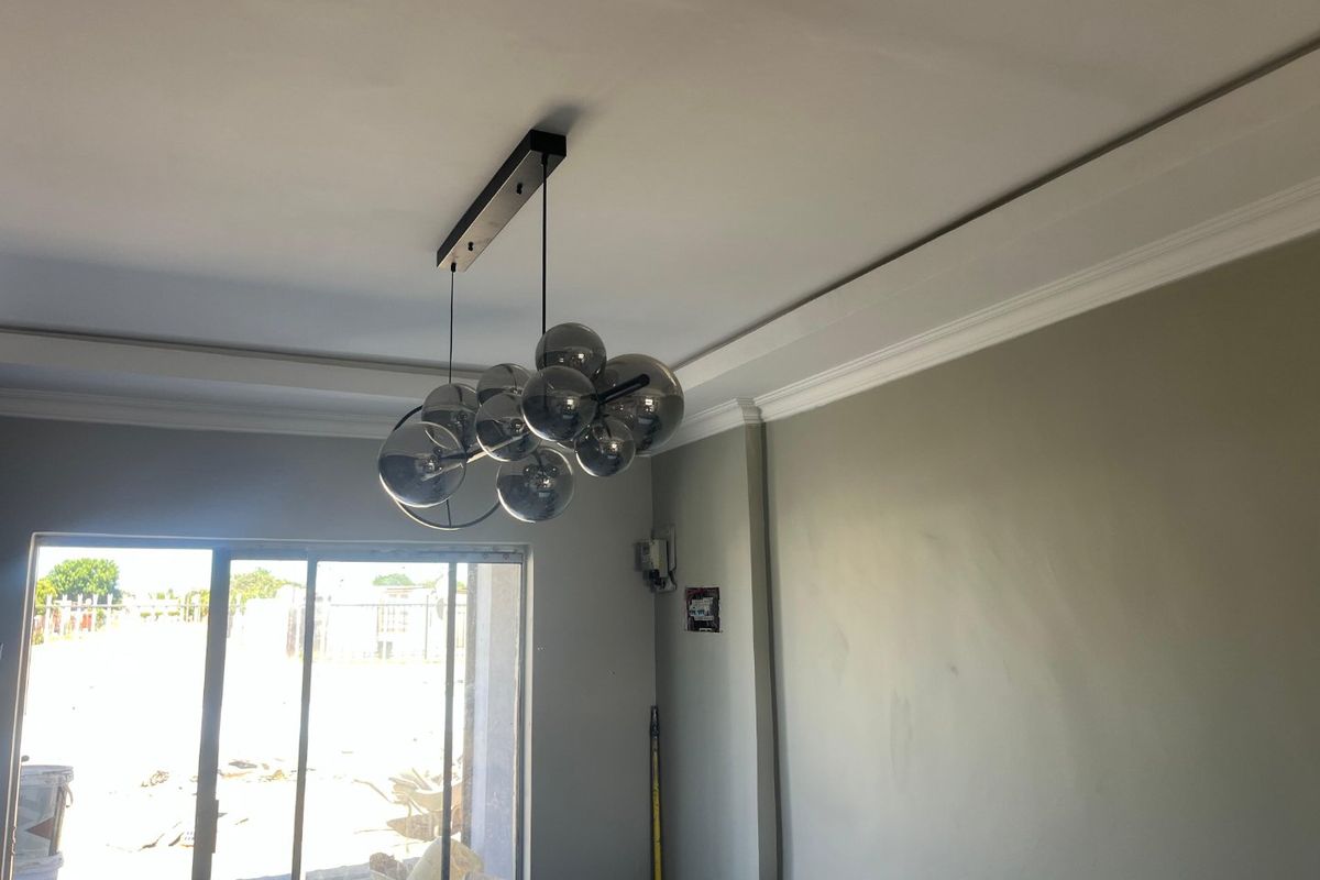 An empty living room featuring crown molding, a modern pendant light fixture, and a sliding glass door leading to the exterior.