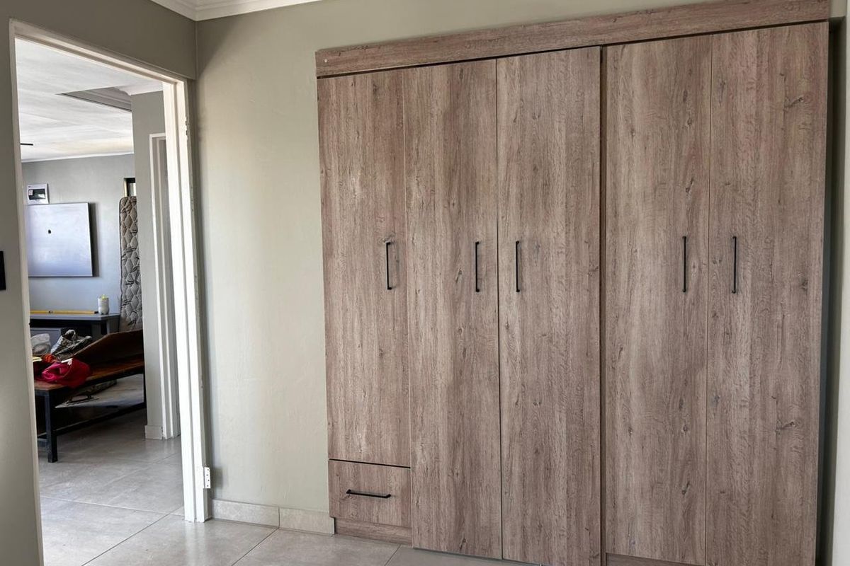 A bedroom featuring modern wood-look built-in cupboards and neutral tiled flooring, offering a clean and functional storage solution.
