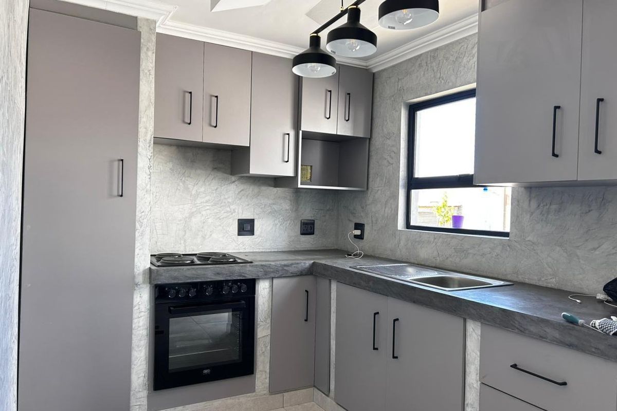 Modern kitchen featuring sleek grey cabinetry, stone-look countertops, integrated oven and hob, and contemporary pendant lighting in a clean, well-maintained space.