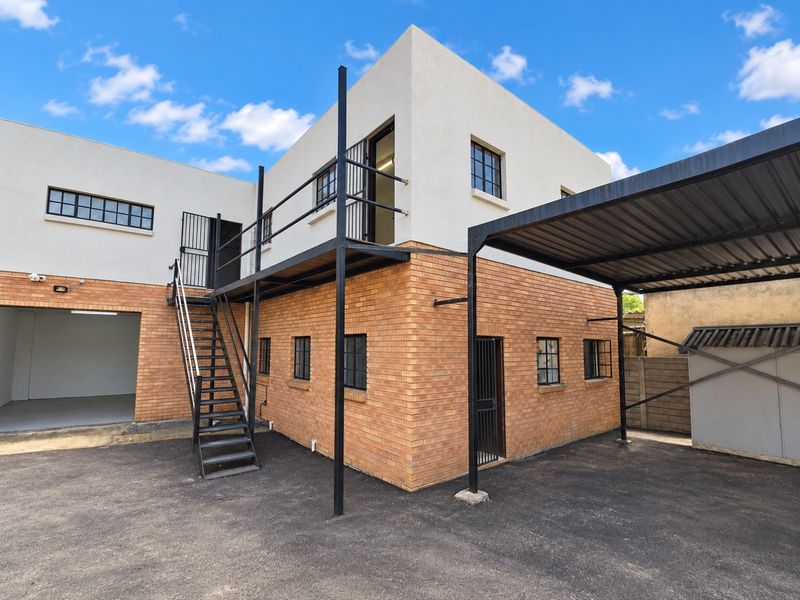 Rear view of a commercial building featuring a brick and rendered facade, external metal staircase, balcony access, and a covered carport area.