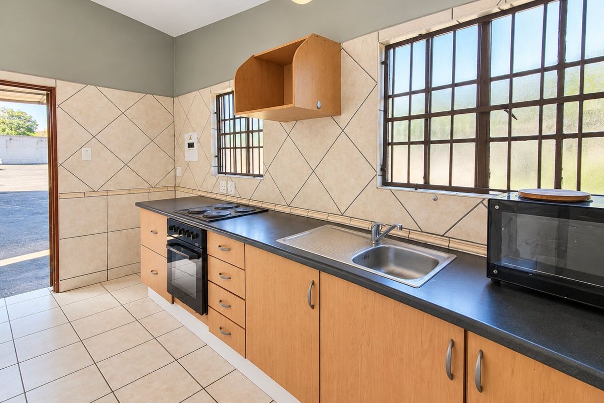 A functional kitchen featuring built-in wooden cabinetry, a stainless steel sink, integrated oven and hob, and tiled finishes throughout.
