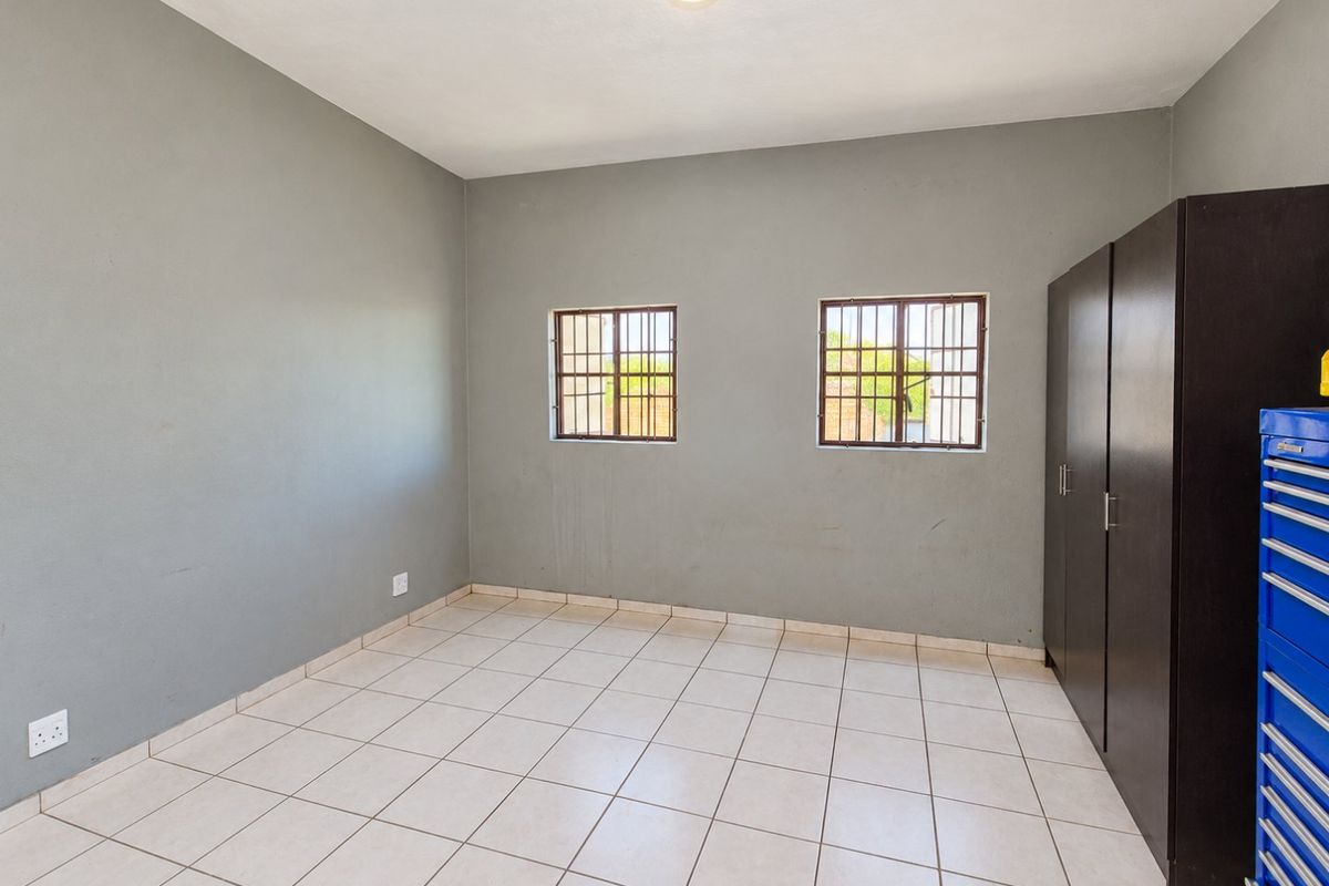 A clean, empty bedroom featuring neutral grey walls, light-colored floor tiles, security-barred windows, and a built-in storage cupboard.