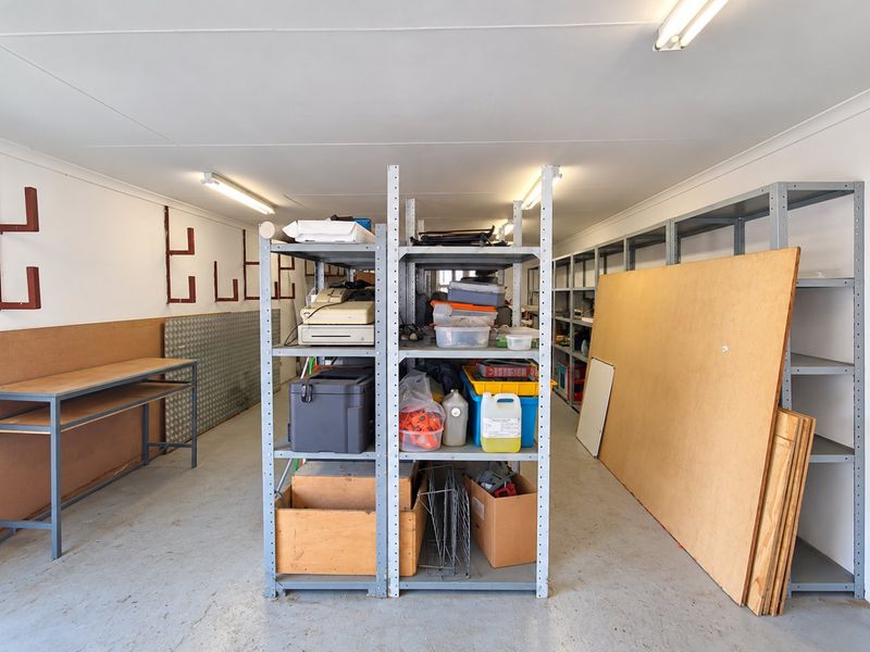 A functional utility or storage space featuring concrete flooring, metal shelving units, a workbench, and overhead fluorescent lighting.