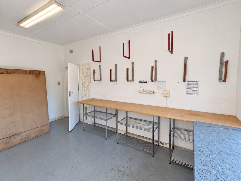 A functional utility or workshop space featuring a built-in workbench, wall-mounted storage brackets, and durable painted concrete flooring, suitable for various commercial storage or prep needs.