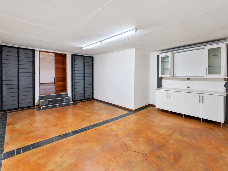 A spacious utility room featuring stained concrete flooring, built-in cabinetry, and direct access to an adjacent room via a small set of tiled steps.