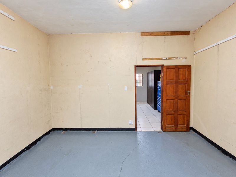 An empty utility or storage room featuring a painted concrete floor, timber door, and basic electrical infrastructure, requiring cosmetic updates to the walls and flooring.