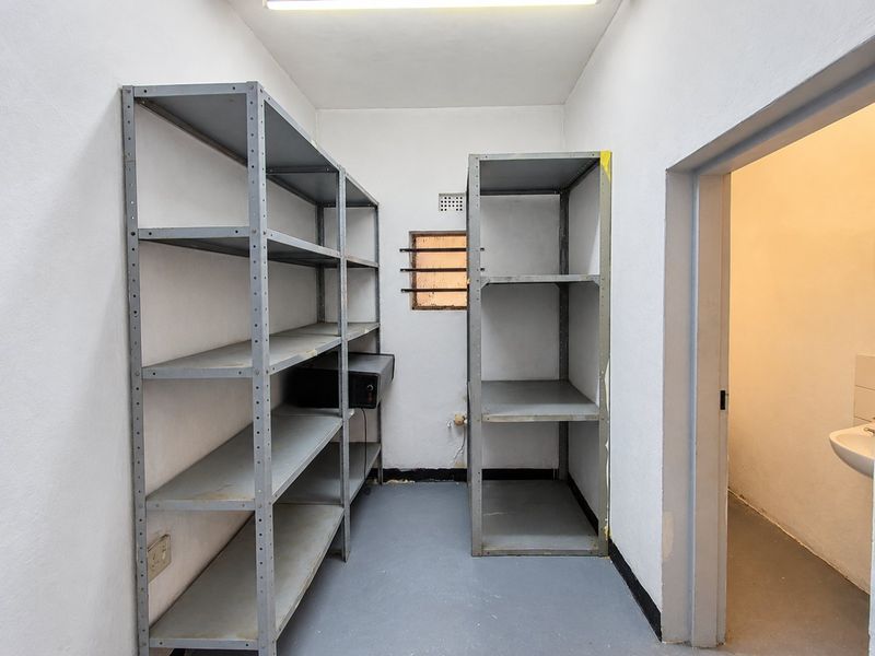 A functional utility or storage room featuring painted walls, durable flooring, and a small window with security bars.