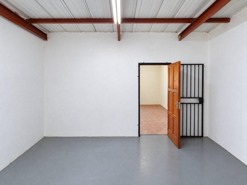 A clean, functional utility space featuring exposed steel beams, a corrugated metal ceiling, and a secure entrance gate leading to an adjacent room.