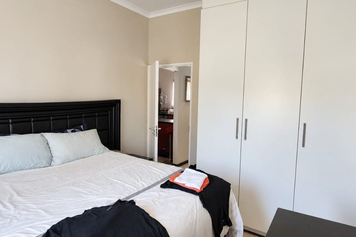 A well-maintained bedroom featuring neutral walls, laminate flooring, and ample built-in cupboard storage, with a view into the adjacent kitchen area.