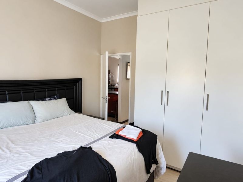 A well-maintained bedroom featuring neutral walls, laminate flooring, and ample built-in cupboard storage, with a view into the adjacent kitchen area.