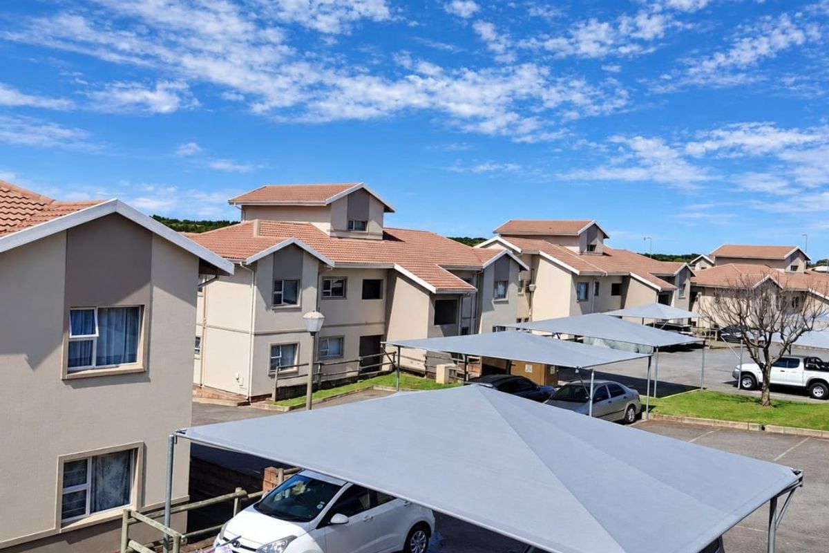 Exterior view of the apartment complex featuring paved parking bays with shade cloth carports and tiled roof architecture.