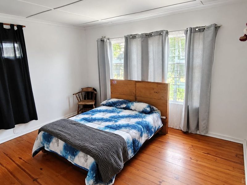 A bedroom featuring polished hardwood flooring, large multi-pane windows, and a simple ceiling panel finish.