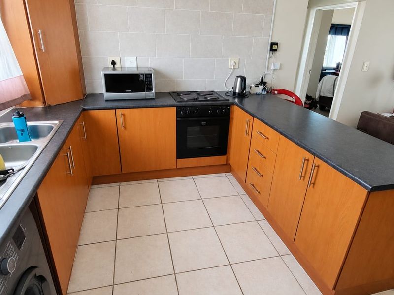 A functional kitchen featuring wood-look cabinetry, dark laminate countertops, built-in oven with electric hob, and neutral tiled flooring and backsplash.