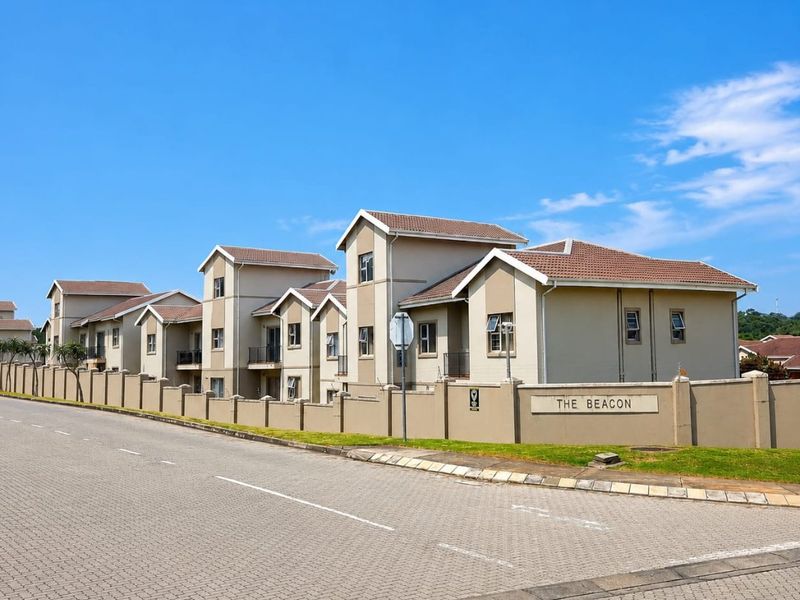 Street view of The Beacon apartment complex, featuring multi-story residential buildings with tiled roofs and a secure perimeter wall.