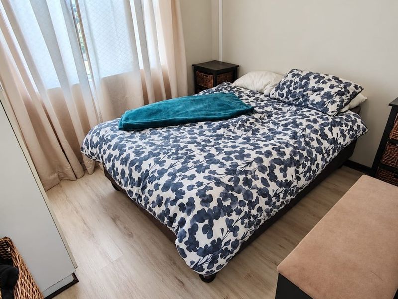 A compact bedroom featuring light-toned laminate flooring and large windows with installed curtain tracks, providing a neutral foundation for interior design.