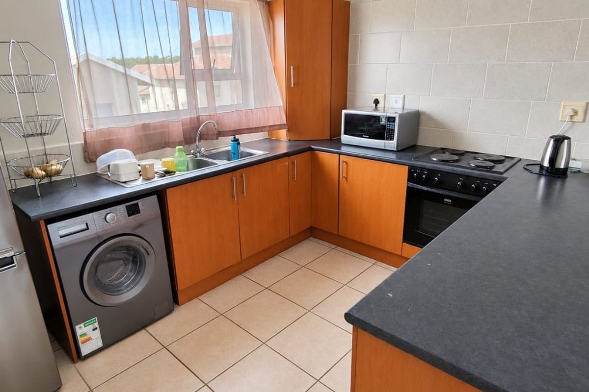 A functional kitchen featuring wood-finish cabinetry, dark laminate countertops, tiled splashbacks, and a built-in oven with electric hob.