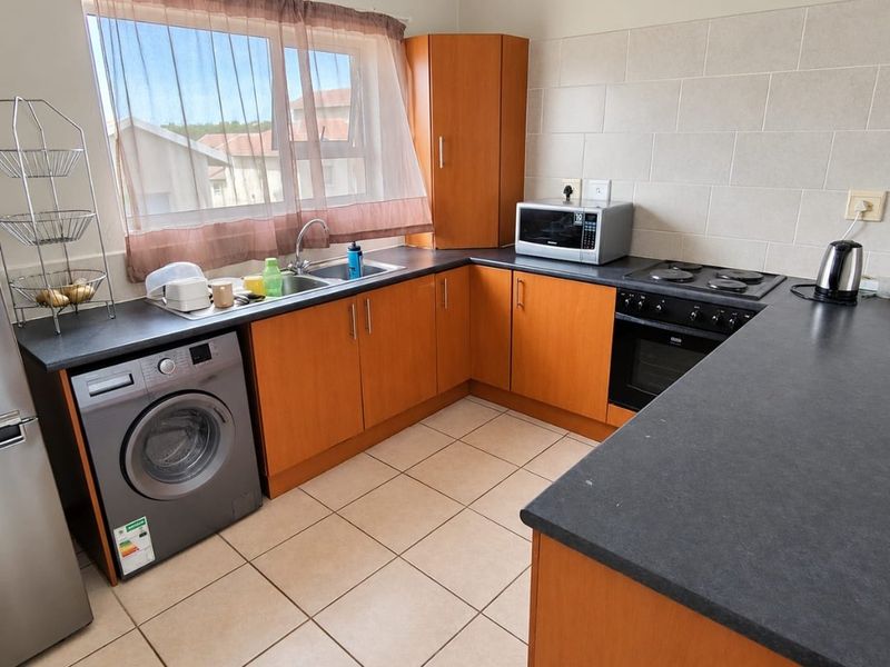 A functional kitchen featuring wood-finish cabinetry, dark laminate countertops, tiled splashbacks, and a built-in oven with electric hob.