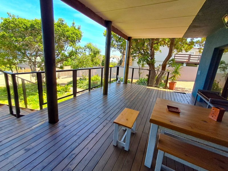A spacious covered timber deck featuring a glass balustrade, overlooking a landscaped garden area.