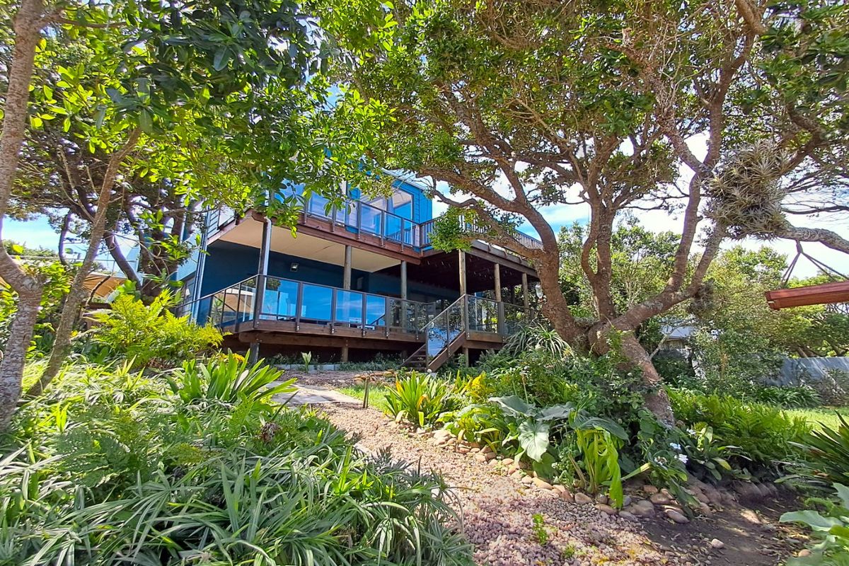 Rear view of the property featuring multi-level timber decking with glass balustrades, set within a lush, mature landscaped garden with a gravel pathway.