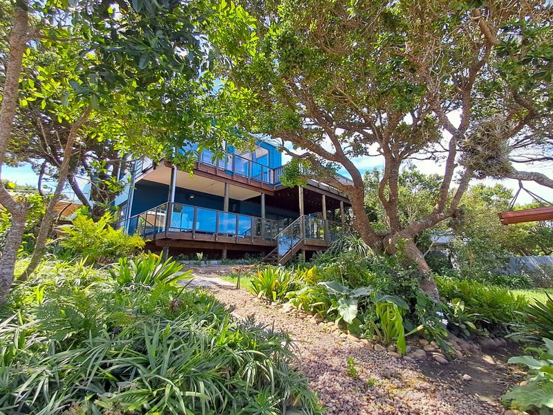 Rear view of the property featuring multi-level timber decking with glass balustrades, set within a lush, mature landscaped garden with a gravel pathway.