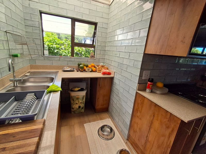 A modern kitchen featuring light blue subway tile backsplash, wood-finish cabinetry, stone-look countertops, and a functional stainless steel double sink under a window.