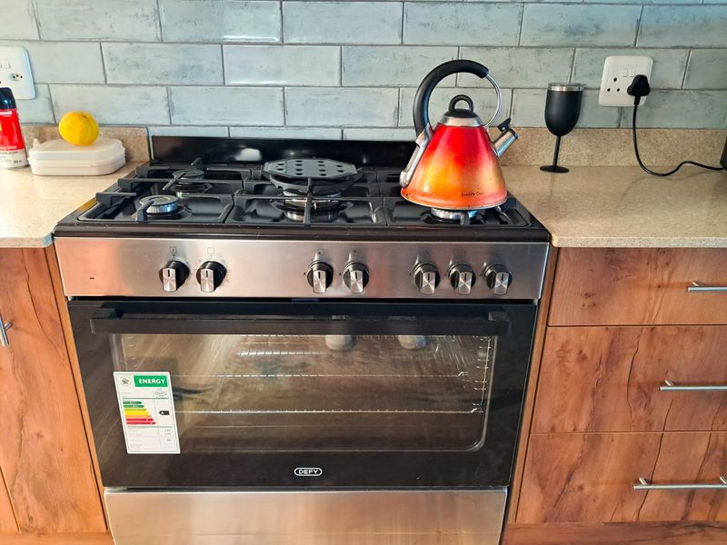 A well-maintained kitchen area featuring a stainless steel Defy gas stove and oven, complemented by stone countertops and a stylish subway tile backsplash.