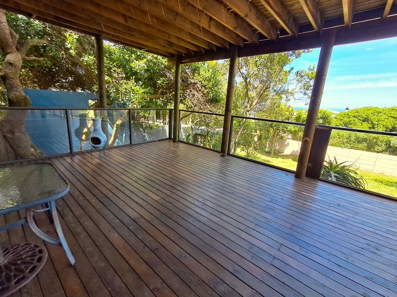 A spacious covered timber deck featuring a glass balustrade, exposed wooden rafters, and scenic garden views, ideal for outdoor entertaining.