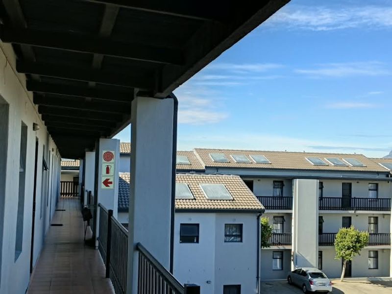An exterior covered walkway and balcony area overlooking the apartment complex courtyard with views of the surrounding neighborhood.