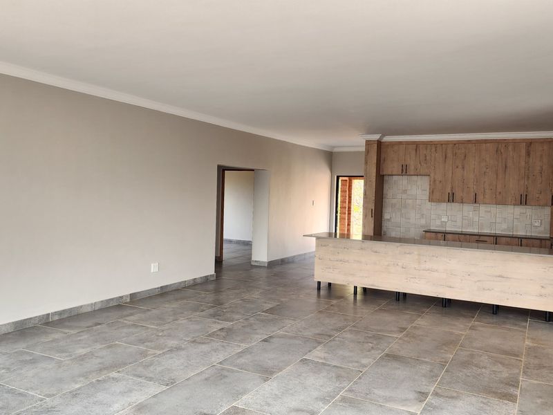 Spacious open-plan living area featuring a modern kitchen with wood-finish cabinetry, a central island, and neutral tiled flooring throughout.