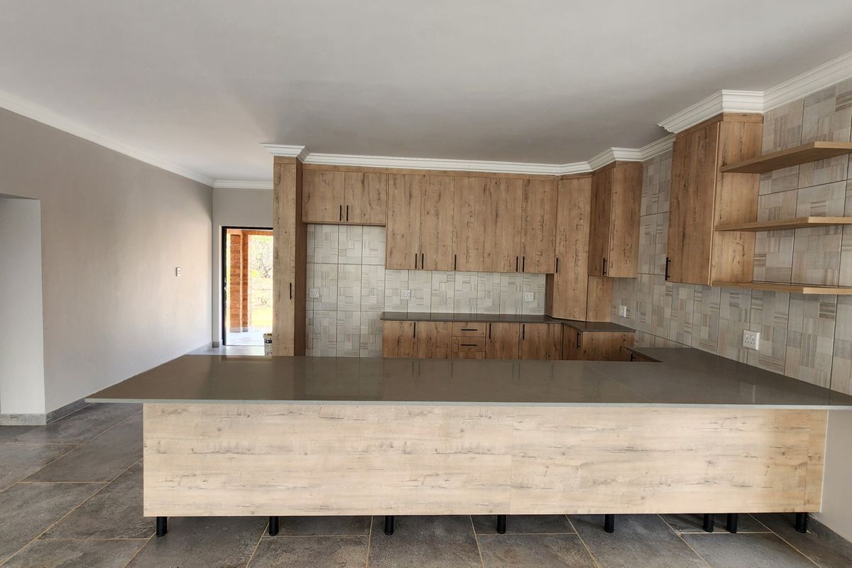 Modern open-plan kitchen featuring light wood-grain cabinetry, stone countertops, a functional island, and stylish tiled backsplash with integrated open shelving.