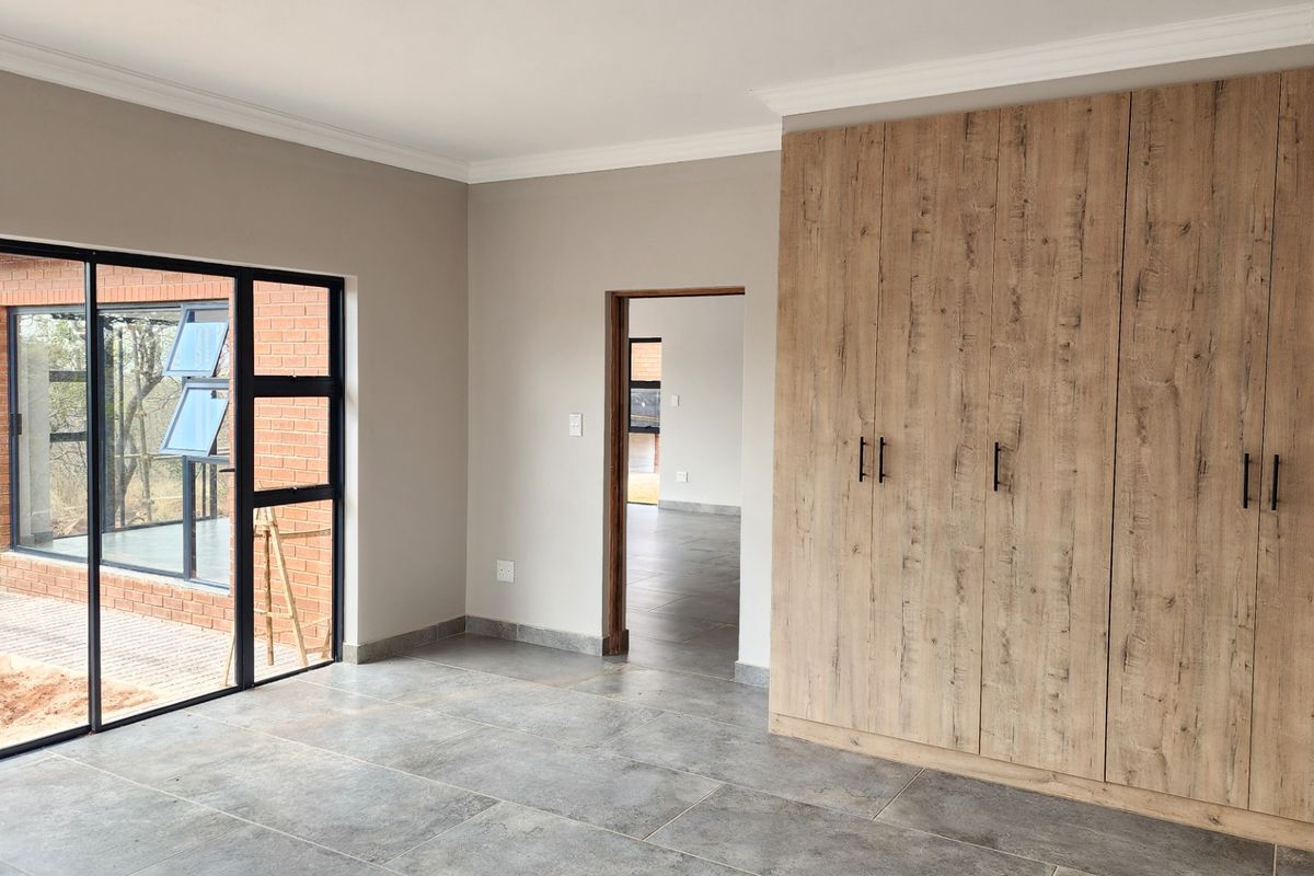 A bright, modern bedroom featuring large built-in wooden cupboards, sleek tiled flooring, and a sliding glass door providing access to the exterior.