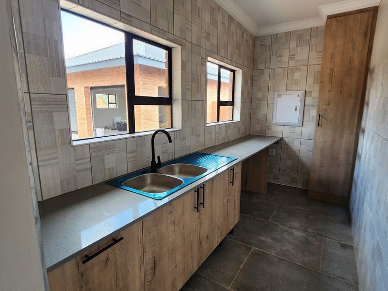 Modern scullery featuring stone countertops, double sink with black mixer tap, ample built-in cabinetry, and full-height pantry storage with neutral wall and floor tiling.