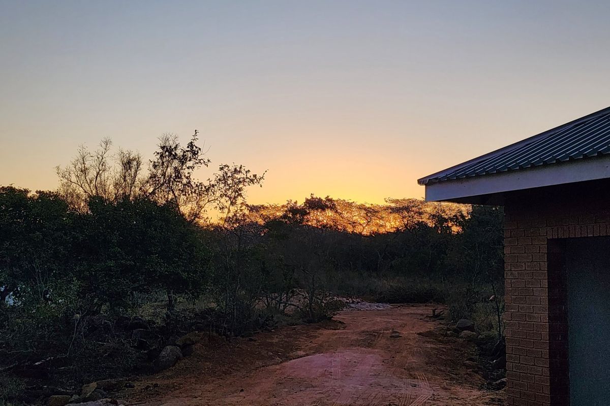 A view of the property exterior at sunset, featuring a brick wall and metal roofing overlooking a natural landscape.